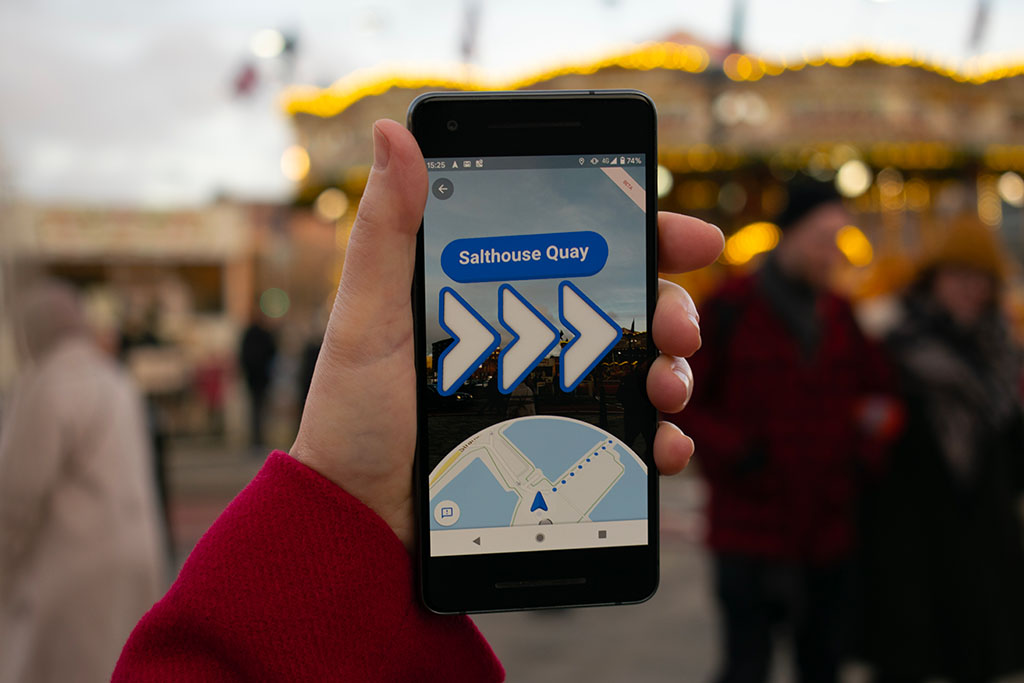 Google maps AR. Na mobilu jsou ukázané šipky, kudy se vydat.